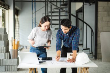 Asyalı erkek ve kadın mimarlar kapalı bir inşaat alanının planlarını gözden geçiriyorlar. Modern bir mimari proje için takım çalışması, planlama ve mühendislik devam ediyor.