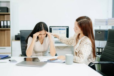 Asyalı kadın, sıkıntılı iş arkadaşını ofisinde rahatlatıyor. Profesyonel ortamlarda işyeri stresi, tükenme, empati ve duygusal destek kavramı.