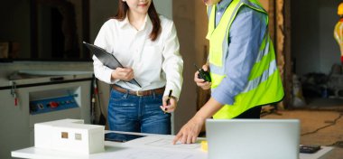 Modern ofisin masasındaki inşaat sahasında mimari projeyle büyük çizimlere yansıyan yaratıcı mimar