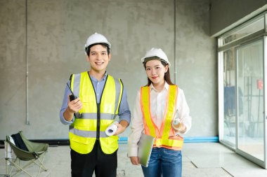 Tam teşekküllü proje planları ve dizüstü bilgisayarı üzerinde kutlama yapmak için iki sağlam şapka ve güvenlik yelekli inşaat profesyoneli yumruklarını kaldırarak sahada takım çalışması başarısını simgeliyor..