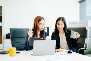 Takım elbiseli iki Asyalı iş kadını modern bir ofis masasında raporları analiz ediyor. Takım çalışması, liderlik ve veri odaklı karar verme sahnesi