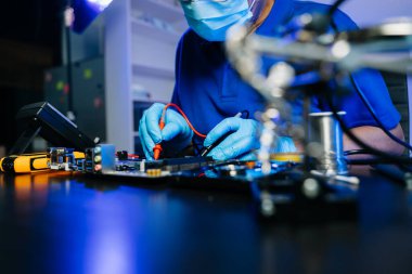 Teknisyen teşhis için çoklu sayaç kullanıyor. Eldivenler, aletler ve donanım donanımı, yüksek teknoloji elektronik tamir alanındaki gerçek insanları gösteriyor.