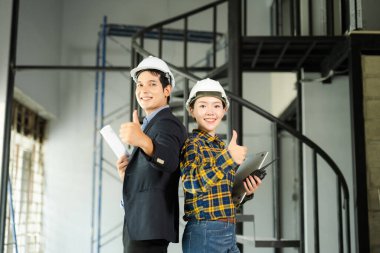 Asyalı iki genç mühendis inşaat alanında güvenle gülümsüyor, işbirliği, güvenlik ve mimari profesyonellik sergiliyorlar..