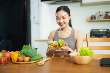 Gülümseyen Asyalı kadın ev mutfağında taze sebze salatası hazırlıyor. Sağlıklı yaşam tarzı, temiz yemek, sağIık ve zindelik gıda hazırlık konsepti..