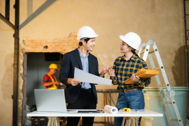 Mühendis ve müvekkil inşaat alanında el sıkışıyor ve başarılı bir anlaşma imzalıyor. Sert şapkalar, planlama araçları ve takım çalışması güven ve başarıyı vurguluyor.