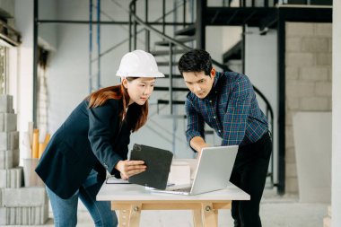 Asyalı mimarlar ve mühendisler kasklar, dizüstü bilgisayarlar ve takım çalışması ile ilgili planları tartışıyorlar. İnşaat, takım çalışması ve projec için ideal