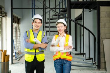 Tam teşekküllü proje planları ve dizüstü bilgisayarı üzerinde kutlama yapmak için iki sağlam şapka ve güvenlik yelekli inşaat profesyoneli yumruklarını kaldırarak sahada takım çalışması başarısını simgeliyor..