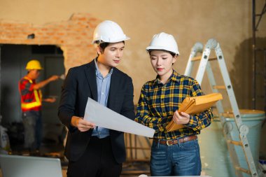 Mühendis ve müvekkil inşaat alanında el sıkışıyor ve başarılı bir anlaşma imzalıyor. Sert şapkalar, planlama araçları ve takım çalışması güven ve başarıyı vurguluyor.