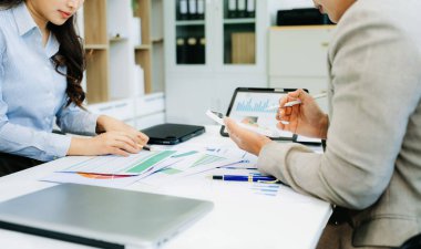 İki profesyonel modern bir ofiste dijital cihazları kullanarak finansal tabloları analiz ediyor..