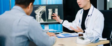 Asyalı doktor, modern klinikteki yaşlı bir hastayla diz röntgeni sonuçlarını tartışıyor. Ortopedik konsültasyon, kemik bakımı, sağlık teşhisi ve güven kavramı.