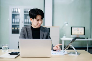 Kendine güvenen genç Asyalı işadamı dizüstü bilgisayardaki mali tabloları analiz ediyor. İşletme, finans, işyeri, başarı ve modern ofis yaşam tarzı konuları için mükemmel