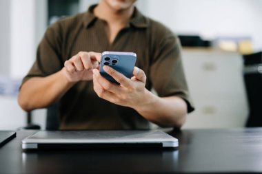 Bilgisayarlı bir masada akıllı telefon kullanan bir adamın yakın çekimi. Modern dijital yaşam tarzı, iş için mükemmel, ve mobil uygulama kavramları.