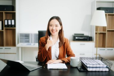 Genç, güzel bir kadın, modern ofisteki çalışan beyaz masada otururken tablet ve dizüstü bilgisayarda yazı yazıyor.