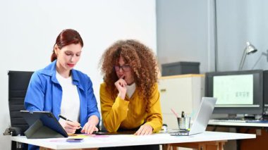 Kadın grafik tasarımcılar ofisteki yaratıcı masada cihazlar kullanıyorlar. Renk paletleri ve tasarım araçlarıyla çevrili 
