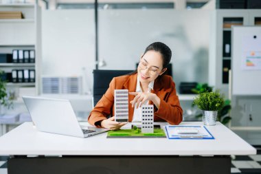 Masada dizüstü bilgisayar ve tabletle çalışan olgun bir emlakçı ve yanında da küçük bir ev..