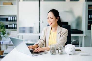 Sırıtkan Asyalı iş kadını elinde domuz kumbarasıyla, yeni finansal fikirleri, yenilikleri ve tasarrufları sembolize ediyor. Finans, iş ve yatırım kavramları için mükemmel.