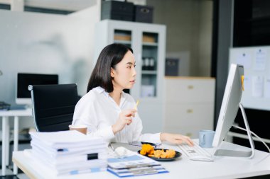 Asyalı iş kadını ofiste birden fazla iş yapıyor, telefonda kızarmış tavuk yiyor. Stres, aşırı çalışma, çoklu görev ve yoğun iş hayatı konsepti için mükemmel..