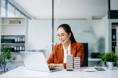 Masada dizüstü bilgisayar ve tabletle çalışan olgun bir emlakçı ve yanında da küçük bir ev..