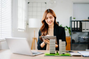 Asyalı emlakçı, emlak satışları, yatırım, anlaşma ve iş görüşmelerini temsilen modern ofisteki konut modelleriyle sözleşme gösterip açıklıyor..