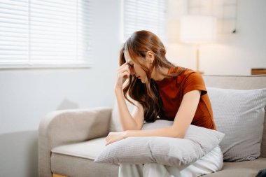 Oturma odasında kanepede oturan Asyalı kadın, stresli hissediyor.