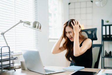 Öfkeli iş kadını iş yerinde stresli ve bunalmış, dizüstü bilgisayarda hayal kırıklığı yaşıyor, ofis baskısını, tükenmeyi ve son teslim tarihi endişesini simgeliyor.