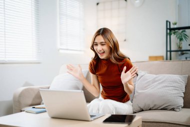 Evdeki video görüşmesi sırasında kulaklık takan, gülümseyen ve el sallayan neşeli Asyalı kadın. Modern iletişim, arkadaşlık ve uzak bağlantı kavramı.