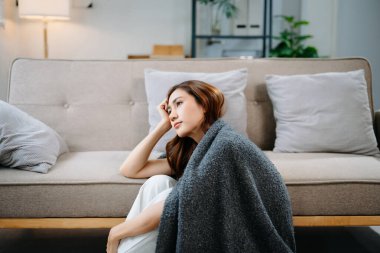 Üzgün Asyalı kadın battaniyeye sarılmış, başı dertteyken yerde oturuyor. Stres, endişe, depresyon, tükenme ve zihinsel sağlık sorunları kavramı.
