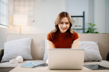 Evde dizüstü bilgisayarla çalışırken gülümseyen neşeli Asyalı kadın. Modern uzaktan çalışma, çevrimiçi öğrenme ve kendine güven ve yaratıcılık içeren serbest yaşam tarzı konsepti.