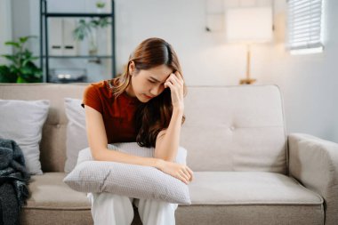 Oturma odasında kanepede oturan Asyalı kadın, stresli hissediyor.
