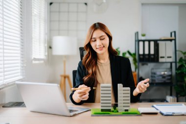 Asyalı emlakçı, emlak satışları, yatırım, anlaşma ve iş görüşmelerini temsilen modern ofisteki konut modelleriyle sözleşme gösterip açıklıyor..