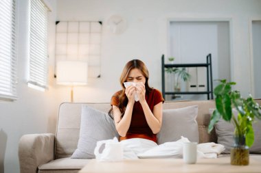 Kanepede battaniyeyle kaplanmış, grip belirtileri gösteren Asyalı bir kadın. Hastalık, sağlık ve iyileşme kavramı. Evde kal, sağlıklı kal.