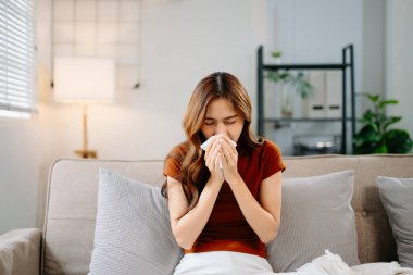 Kanepede battaniyeyle kaplanmış, grip belirtileri gösteren genç bir Asyalı kadın. Hastalık, sağlık ve iyileşme kavramı. Evde kal, sağlıklı kal.