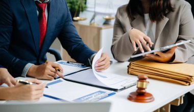 İş adamları sözleşmeleri tartışıyor, kağıtları imzalıyor ve modern bir ofiste dijital cihazlar kullanıyorlar. Takım çalışması, finans, hukuk ve kurumsal başarı kavramı.