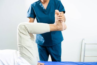 Fizyoterapist, iyileşme sürecinde hastanın bacak ve bilek hareket terapisine yardımcı oluyor. Tıbbi bakım, hareketlilik eğitimi ve kas rehabilitasyonu.