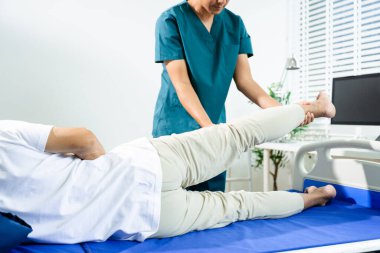 Erkek fizyoterapist, rehabilitasyon sırasında hasta için bacak esneme hareketleri yapar. Klinik tedavi ortamında taşınabilirlik desteği, ortak bakım ve fizik tedavi..