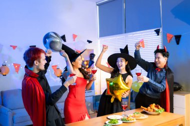 Cadılar Bayramı 'nda cadılar ve şeytanlar gibi giyinmiş arkadaşlarla neşeli bir cadılar bayramı kutlaması, pizza paylaşımı, kahkaha ve canlı kapalı bir parti sahnesinde şenlikli içecekler..