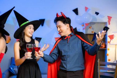 Cadılar Bayramı 'nda cadılar ve şeytanlar gibi giyinmiş arkadaşlarla neşeli bir cadılar bayramı kutlaması, bardakları tokuşturma, gülümseme ve canlı bir parti ortamında şenlikli yemeklerden keyif alma..