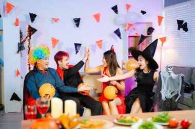 Cadı, palyaço, şeytan ve vampir kostümlü neşeli arkadaşlar güler, beşlik çakar ve Cadılar Bayramı partisinde balkabağı feneri, yiyecek ve içeceklerle kutlarız..