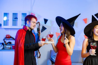 Cadılar Bayramı 'nda cadılar ve şeytanlar gibi giyinmiş arkadaşlarla neşeli bir cadılar bayramı kutlaması, bardakları tokuşturma, gülümseme ve canlı bir parti ortamında şenlikli yemeklerden keyif alma..