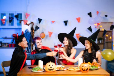 Cadılar Bayramı 'nı içki, balkabağı, pizza ve kapalı bir partide kahkahalarla kutlayan cadı ve şeytan kostümlü mutlu arkadaşlar..