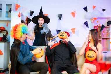 Palyaço, şeytan ve vampir kostümlü neşeli arkadaşlar renkli bir Cadılar Bayramı partisinde balkabağı fenerleri, içkiler ve neşeyle güler ve kutlarlar..