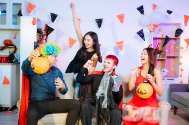 Palyaço, şeytan ve vampir kostümlü neşeli arkadaşlar renkli bir Cadılar Bayramı partisinde balkabağı fenerleri, içkiler ve neşeyle güler ve kutlarlar..