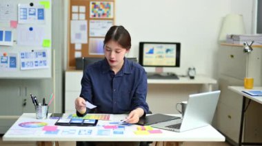 Masa başında çalışan kadın tasarımcı renkli yapışkan notlar düzenliyor