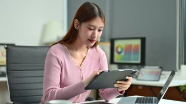 Ofiste otururken tablet kullanan gülümseyen iş kadını.