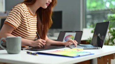 Dizüstü bilgisayarı ve çizimleri olan grafik tableti üzerinde çalışan kadın