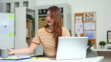 Masada çalışan çekici bir iş kadını. Laptop kullanıyor ve notlar yazıyor.