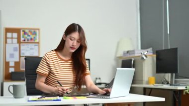 Not defterine yazarken dizüstü bilgisayarda çalışan Asyalı iş kadını