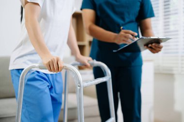 Yürüteç kullanan, iyileşmeyi, taşınabilirlik desteğini ve tıbbi rehabilitasyonu sembolize eden fizyoterapi rehabilitasyonunda bir hastaya yardım eden sağlık uzmanı..