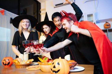 Cadılar Bayramı kostümleri kapalı bir partide kırmızı şarapla kadeh kaldırılır. Balkabakları, yemek ve kutlamalar eğlence, ürkütücü titreşimler ve mevsimlik neşe için ortam oluşturur..