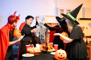 Neşeli ofis Cadılar Bayramı partisi kostüm giymiş iş arkadaşlarıyla, içkiler ve kahkahalarla kutlama, takım çalışmasını teşvik etme ve şenlik ruhu.